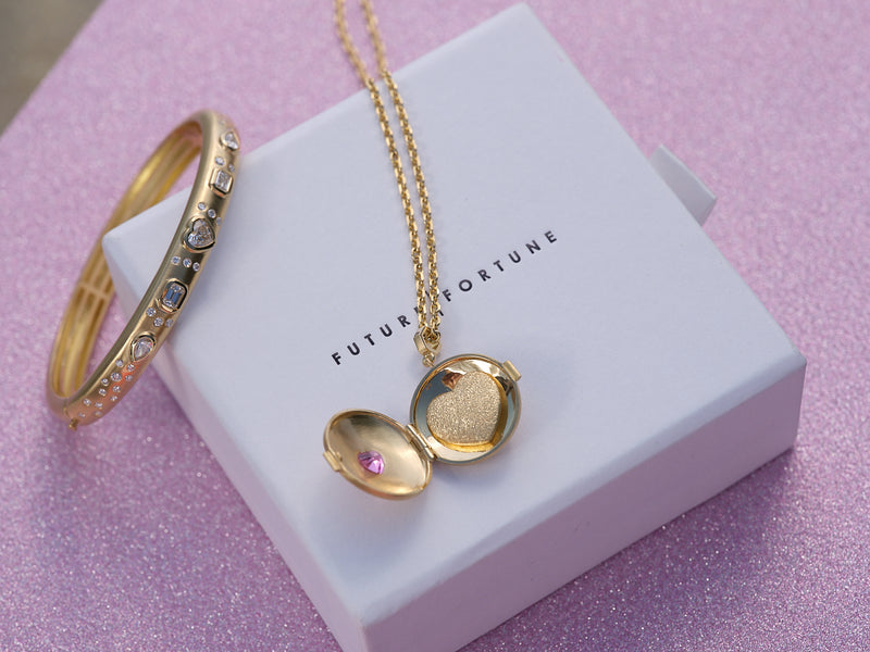 Locket necklace and bangle with white diamonds sitting on a gift box