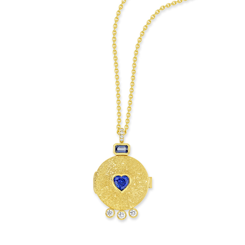 18k yellow gold locket necklace with pavé set white diamond bail. Attaching the bail to the locket is a baguette cut blue sapphire. There is a heart shaped blue sapphire in the center of the locket. At the bottom of the locket are 3 bezel set white diamonds.