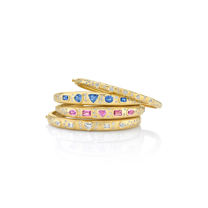 Stack of 4 18k yellow gold bangle bracelets. Top bracelet has all white diamonds, second bracelet has blue sapphires and diamonds, third bracelet has pink sapphires and white diamonds, bottom bracelet has all white diamonds.