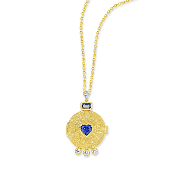 18k yellow gold locket necklace with pavé set white diamond bail. Attaching the bail to the locket is a baguette cut blue sapphire. There is a heart shaped blue sapphire in the center of the locket. At the bottom of the locket are 3 bezel set white diamonds.